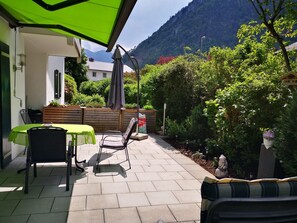 A patio with a table and chairs, a green umbrella, and a view of a mountain. - Fewo Rheinfeld by Interhome (Piding)