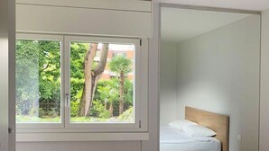 A hotel room with a large window, a bed with white linens, and a radiator below the window. - "Lake Escape", mit Pool by Interhome (MAROGGIA)