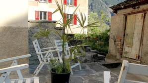 Un patio de piedra con sillas blancas y una planta en maceta.