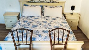 Un dormitorio con cama, dos sillas de madera, una mesita de noche y una lámpara.