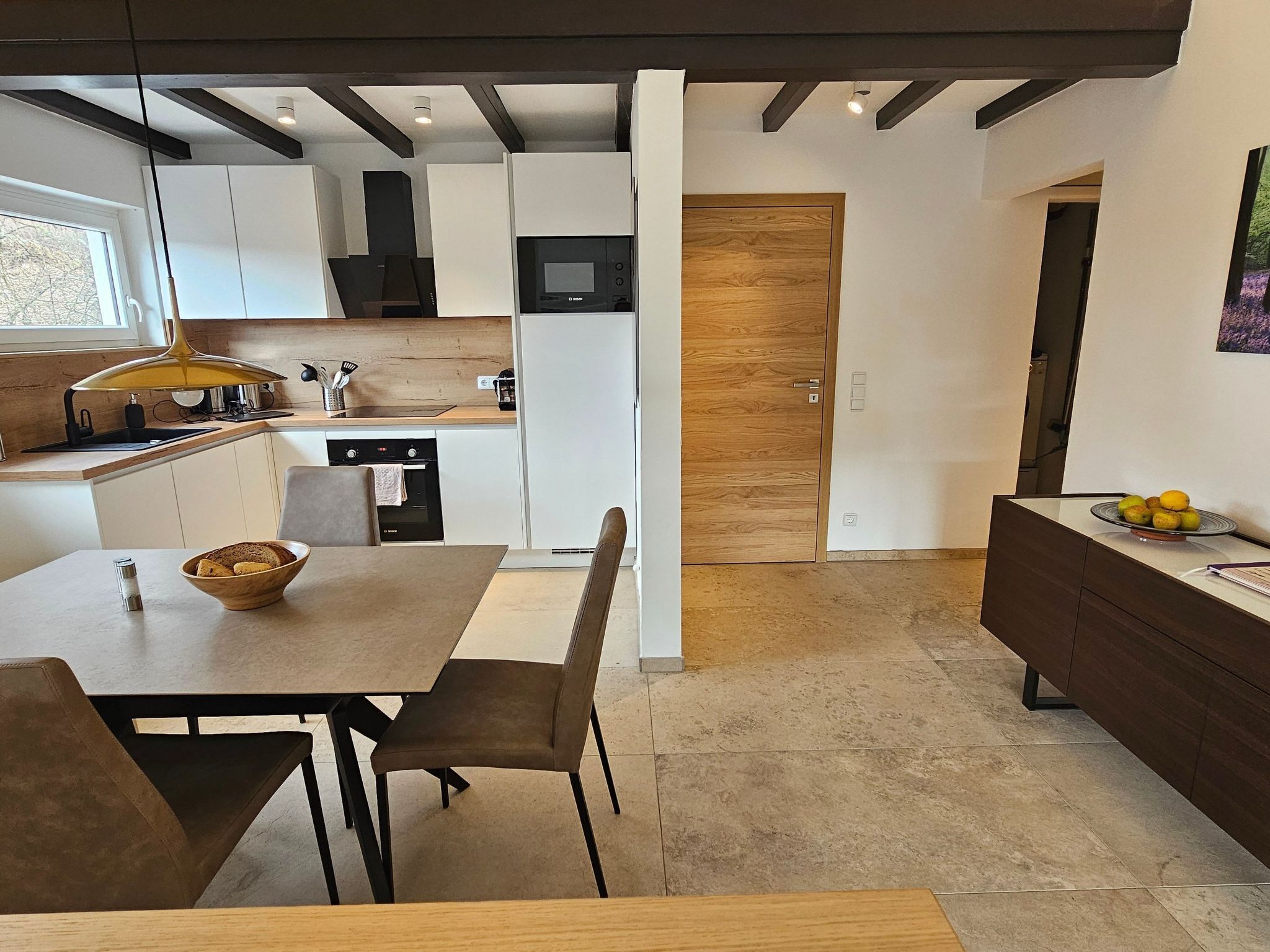 Une cuisine moderne avec des meubles blancs, une porte en bois et un coin repas comprenant une table et des chaises.