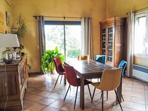 Un comedor con una mesa, sillas, un aparador con puertas de vidrio, una planta en maceta y una ventana con cortinas.