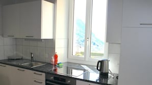 Uma cozinha moderna com armários brancos, uma pia de aço inoxidável e uma janela com vista para o céu.