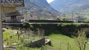 Paisagem rural com um muro de pedra, um pequeno edifício com telhado de telhas e uma ponte ao longe.