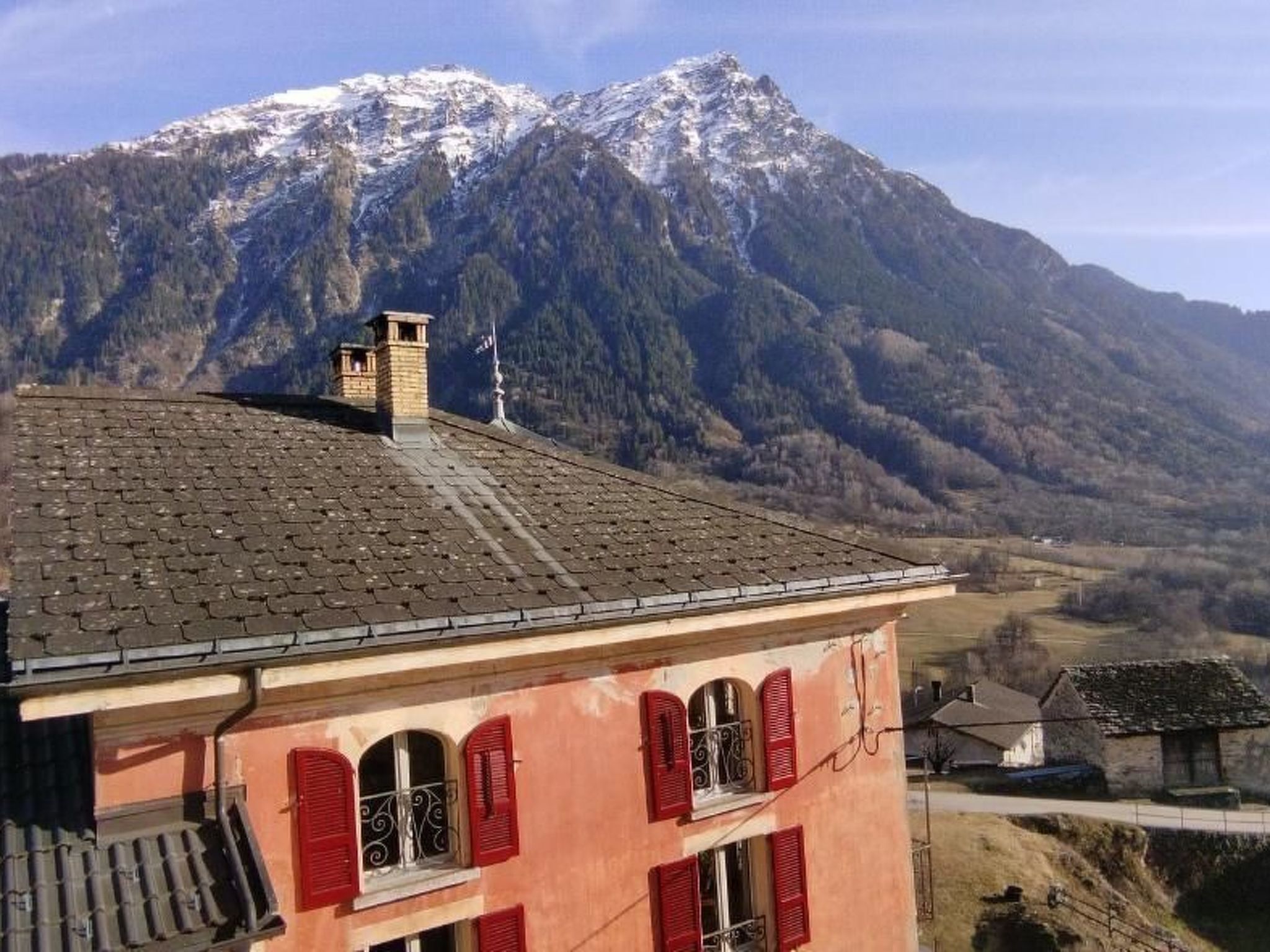 Ein Gebäude mit roten Fensterläden und Schornstein vor einer Kulisse schneebedeckter Berge.