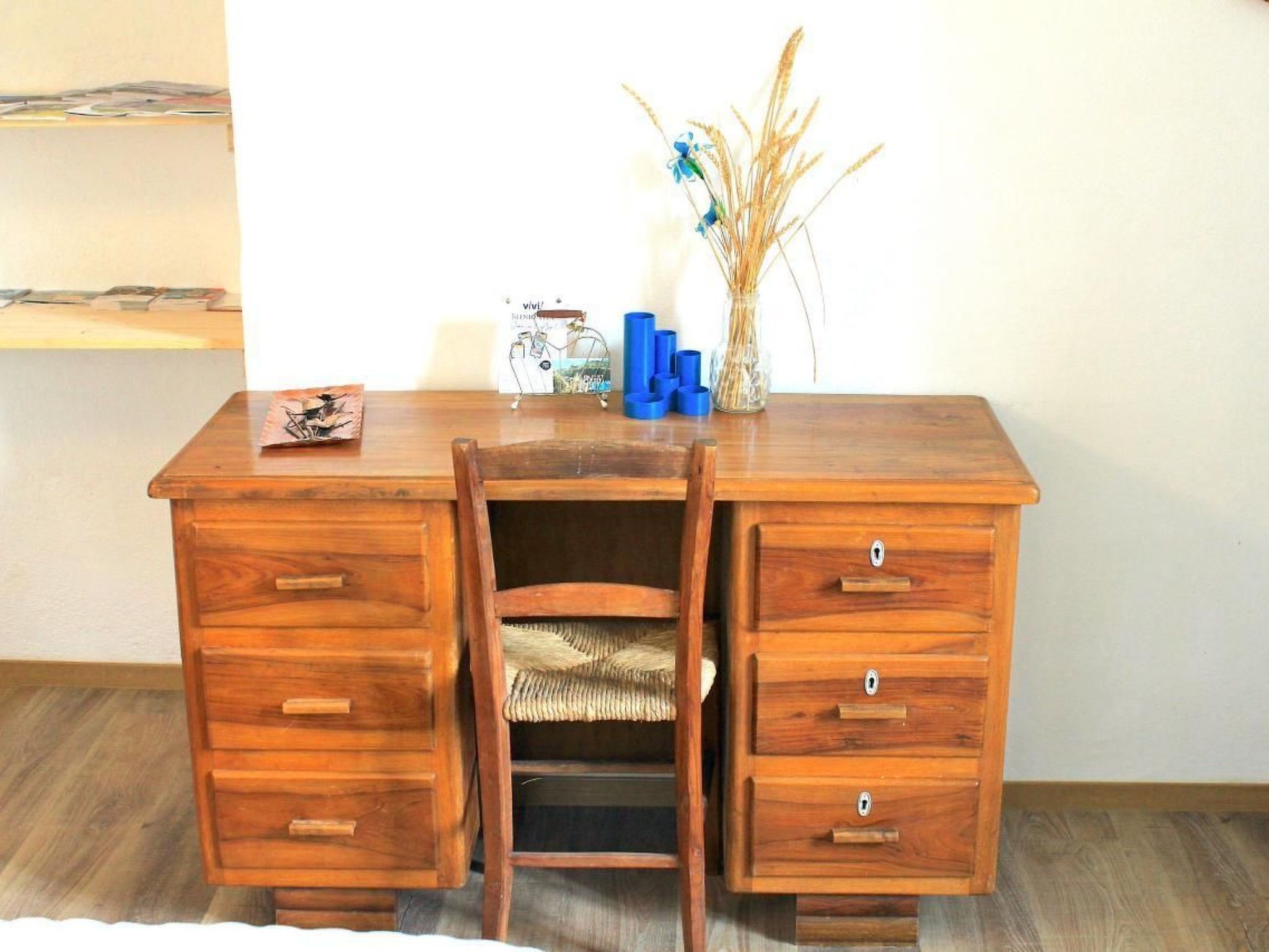 Ein Holztisch mit Stuhl, Schubladen und einer Vase mit getrockneten Pflanzen.