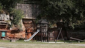 Un terrain de jeux équipé d’un toboggan et de structures d’escalade, avec en arrière-plan des falaises rocheuses et des arbres.