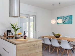Eine moderne Küche mit einer Holzinsel, weißen Schränken und einem Essbereich mit Holztisch und weißen Stühlen.