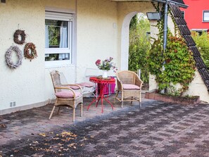 Een terras met rieten stoelen, een tafel met een bloevas en een geplaveid vloertje.