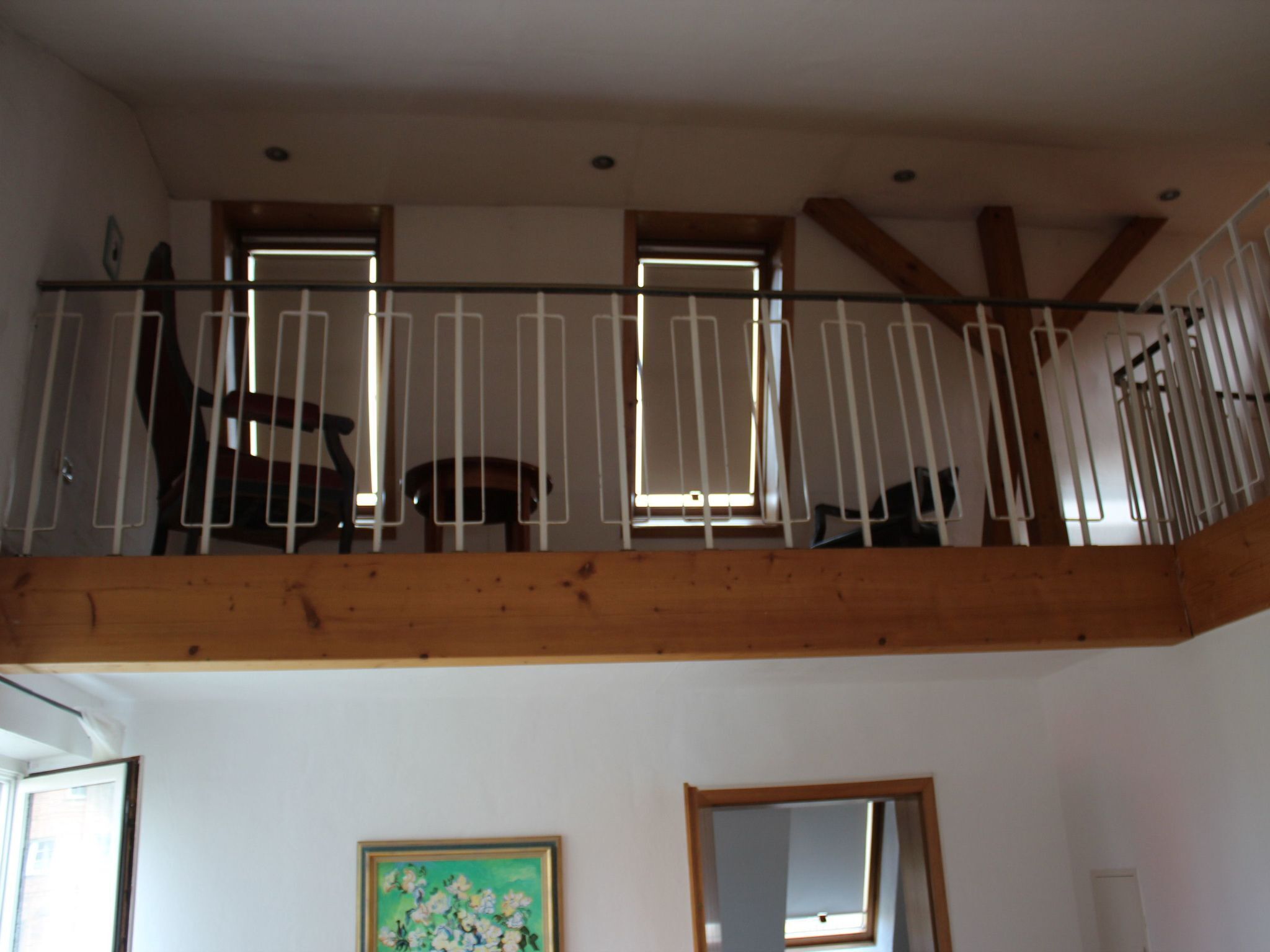 Une pièce avec un balcon en bois, un tableau au mur et une fenêtre donnant sur un beau paysage.