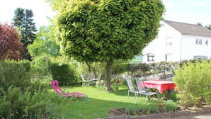 Un jardin avec une pelouse, une table rouge et des chaises en métal.