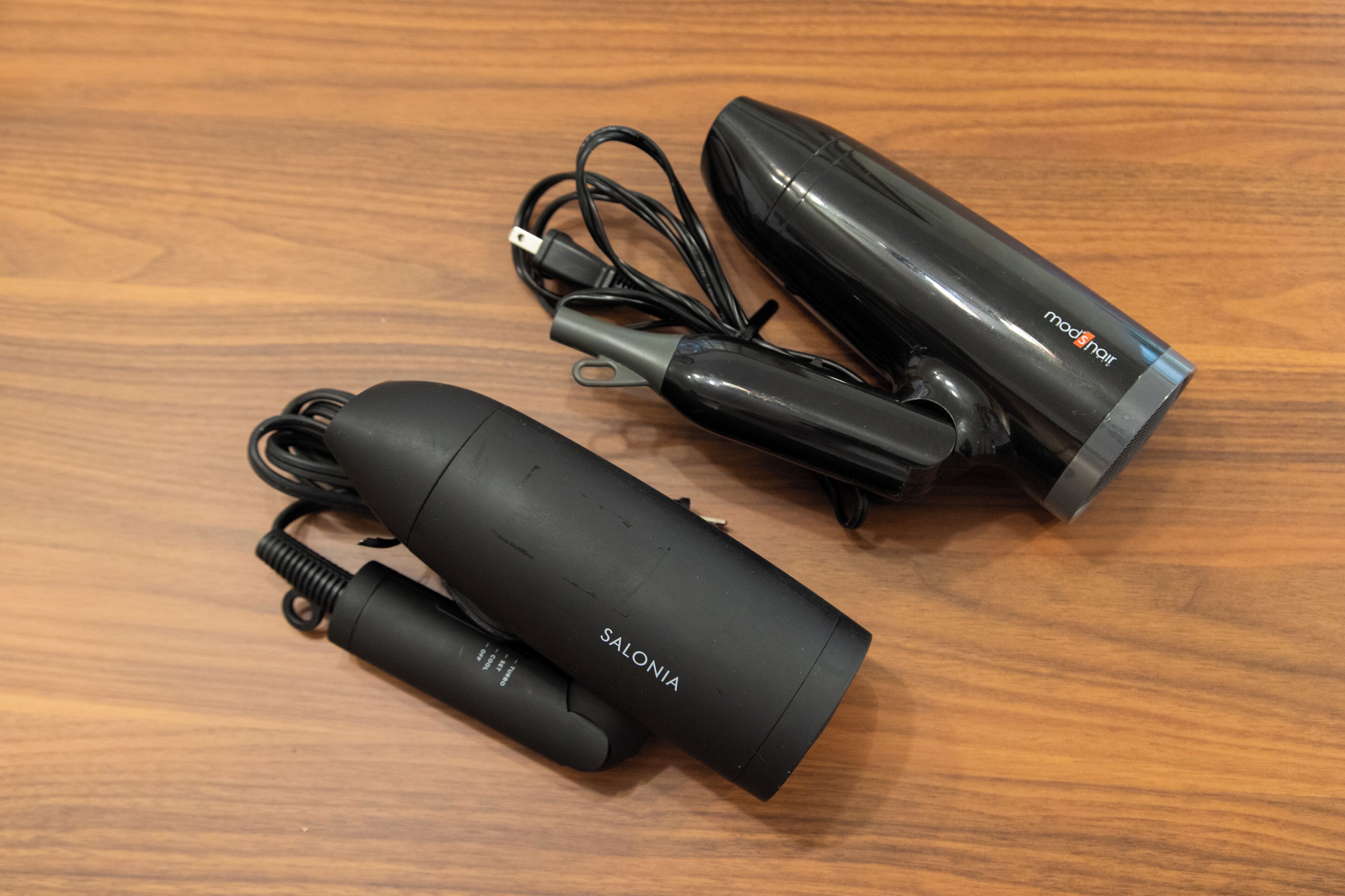 Three black cylindrical devices with cords and a power adapter on a wooden surface.