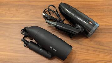 Three black cylindrical devices with cords and a power adapter on a wooden surface.