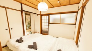 Et traditionelt japansk værelse med tatamimåtter, en stor seng med hvidt sengetøj og en shoji-skydedør.
