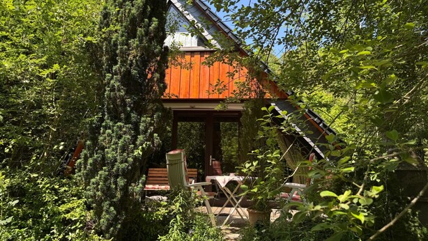 Eine Holzhütte mit geneigtem Dach, umgeben von dichtem Grün.
