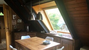Ein gemütlicher Essbereich im Dachgeschoss mit einem Holztisch und weißen Stühlen, einer Hängeleuchte sowie einem Fenster mit Blick auf Grünflächen.