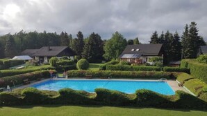 Ein Swimmingpool, umgeben von gepflegten Rasenflächen und Hecken, mit Häusern im Hintergrund.