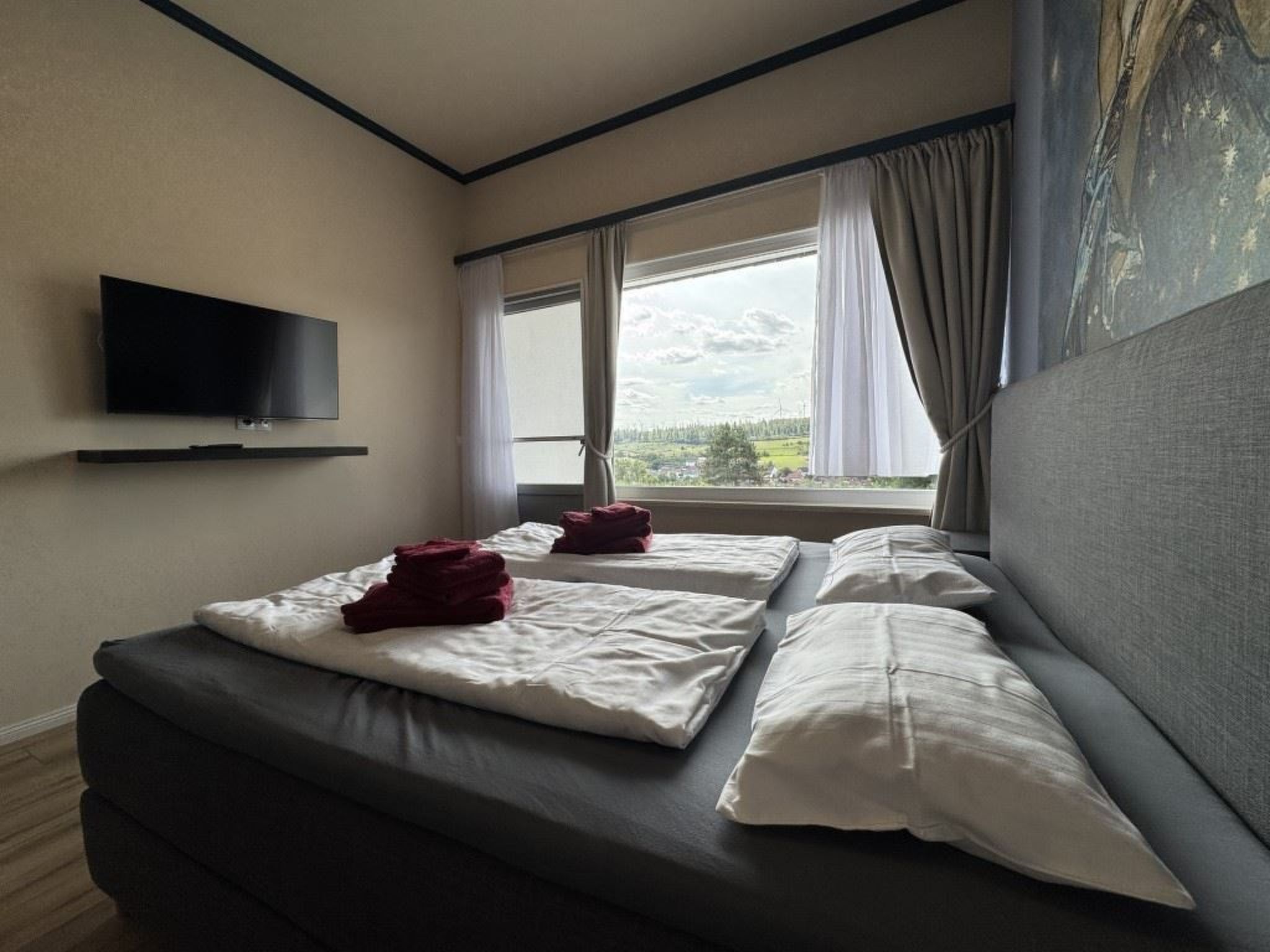 A hotel room with a bed, a flat-screen TV mounted on the wall, and a window with curtains.