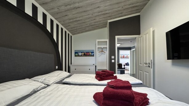 A hotel room with two beds, a large headboard, a painting on the wall, and a TV mounted on the wall. - Feriendorf E44 by Interhome (Husen)