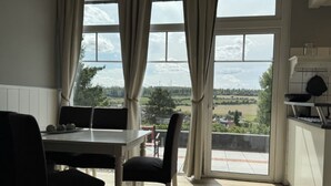A dining area with a table and chairs, large windows with curtains, and a view of a green landscape. - Feriendorf E44 by Interhome (Husen)