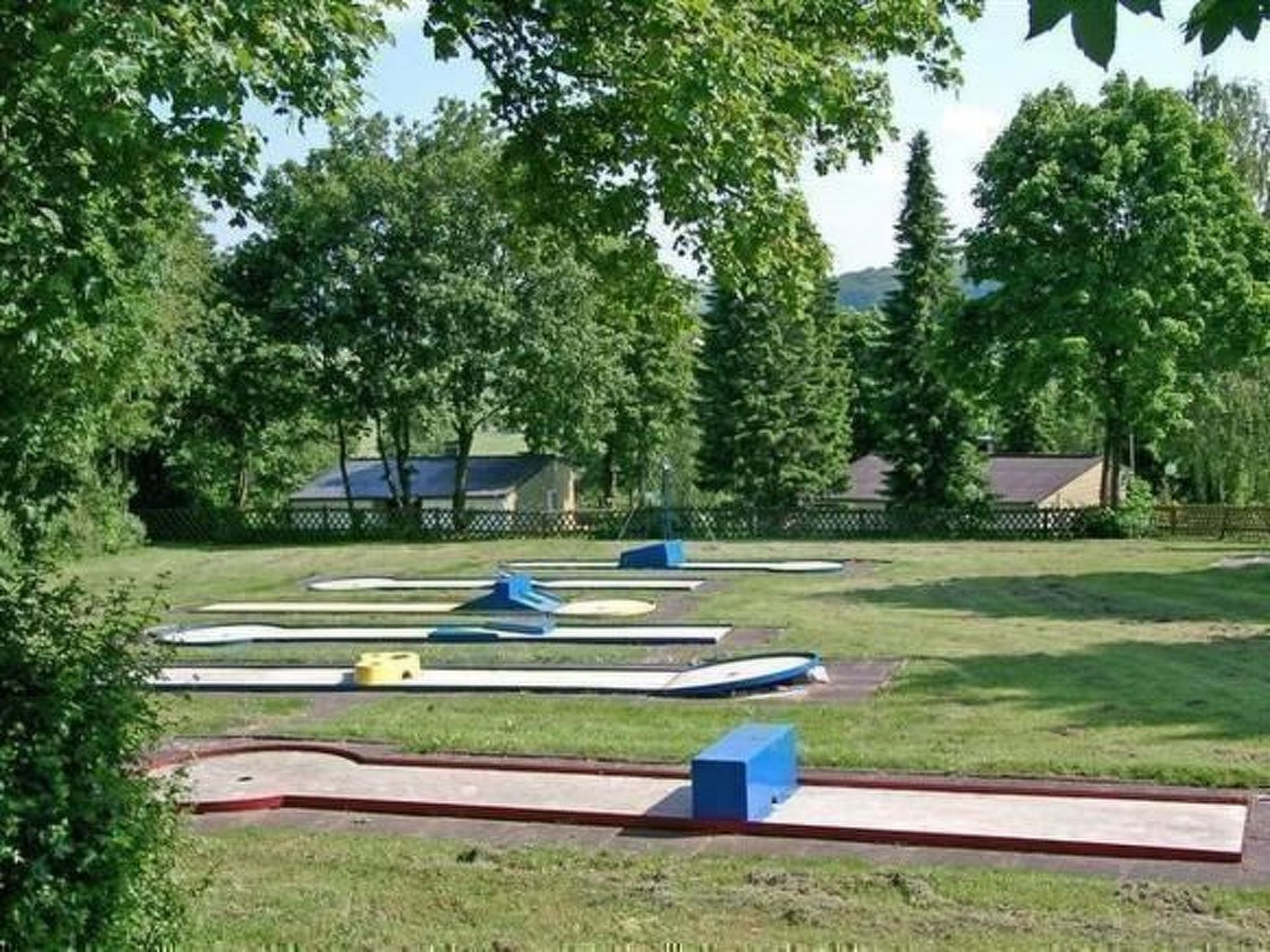 A park with multiple playground equipment, including slides and swings, surrounded by trees and a fenced area.