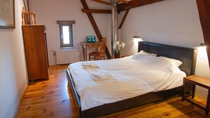 Ein Schlafzimmer mit Holzboden, einem Bett mit weißer Bettwäsche, einem Holztisch, einem Stuhl und einer Heizung.