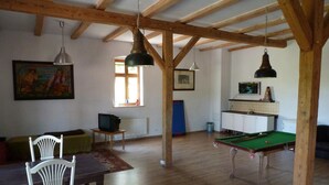 Ein geräumiger Raum mit Holzbalken, einem Billardtisch, einem Fernseher und einem Essbereich mit Stühlen und einem Tisch.