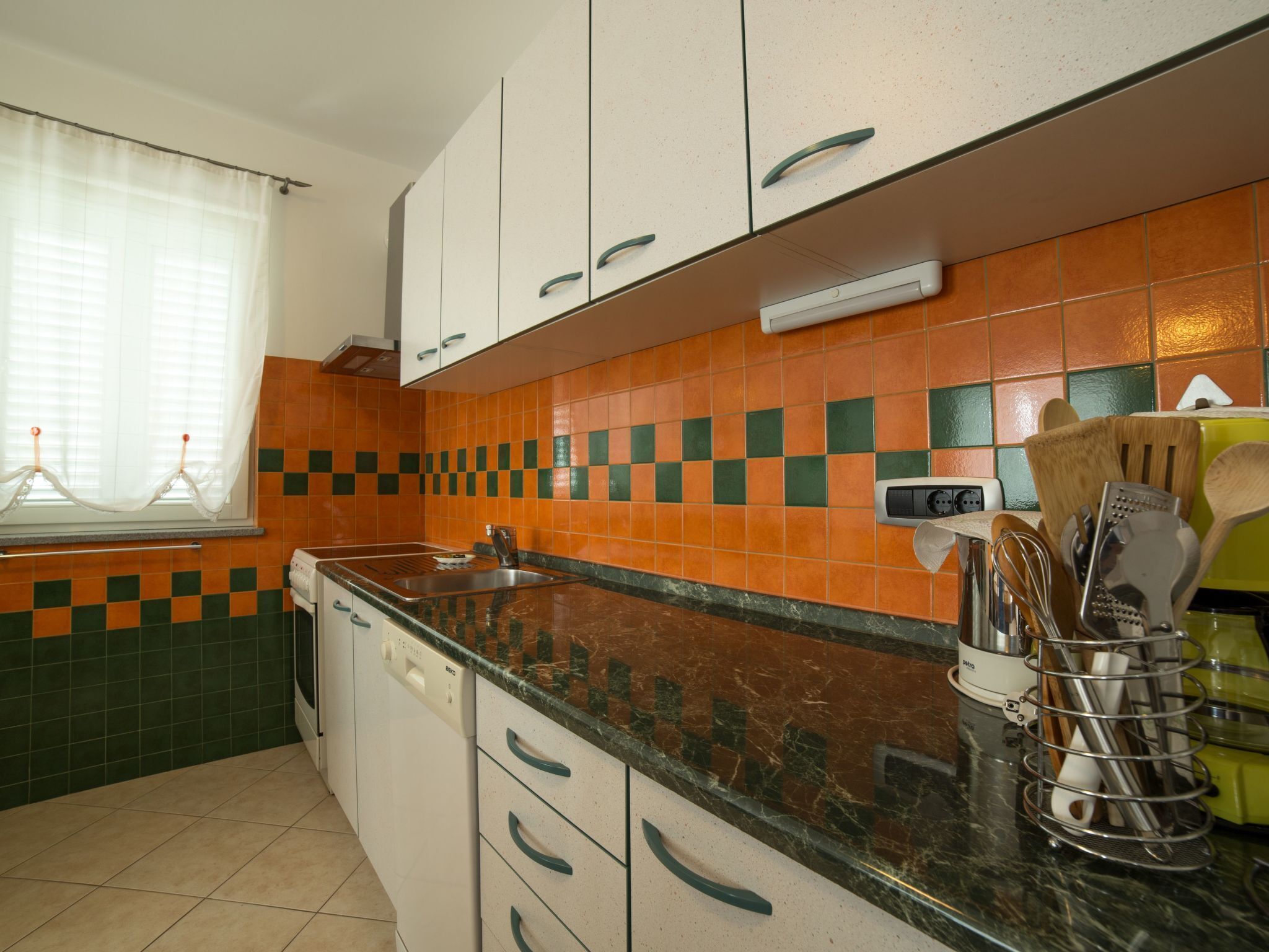 A kitchen with white cabinets, a black countertop, and orange and green checkered backsplash tiles.