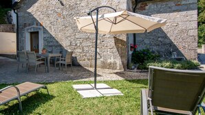 A stone building with a patio area featuring a table and chairs, a large umbrella, and a chair. - Anwesen "Villa Anton" mit eigenem Pool by Interhome (Podgrad)