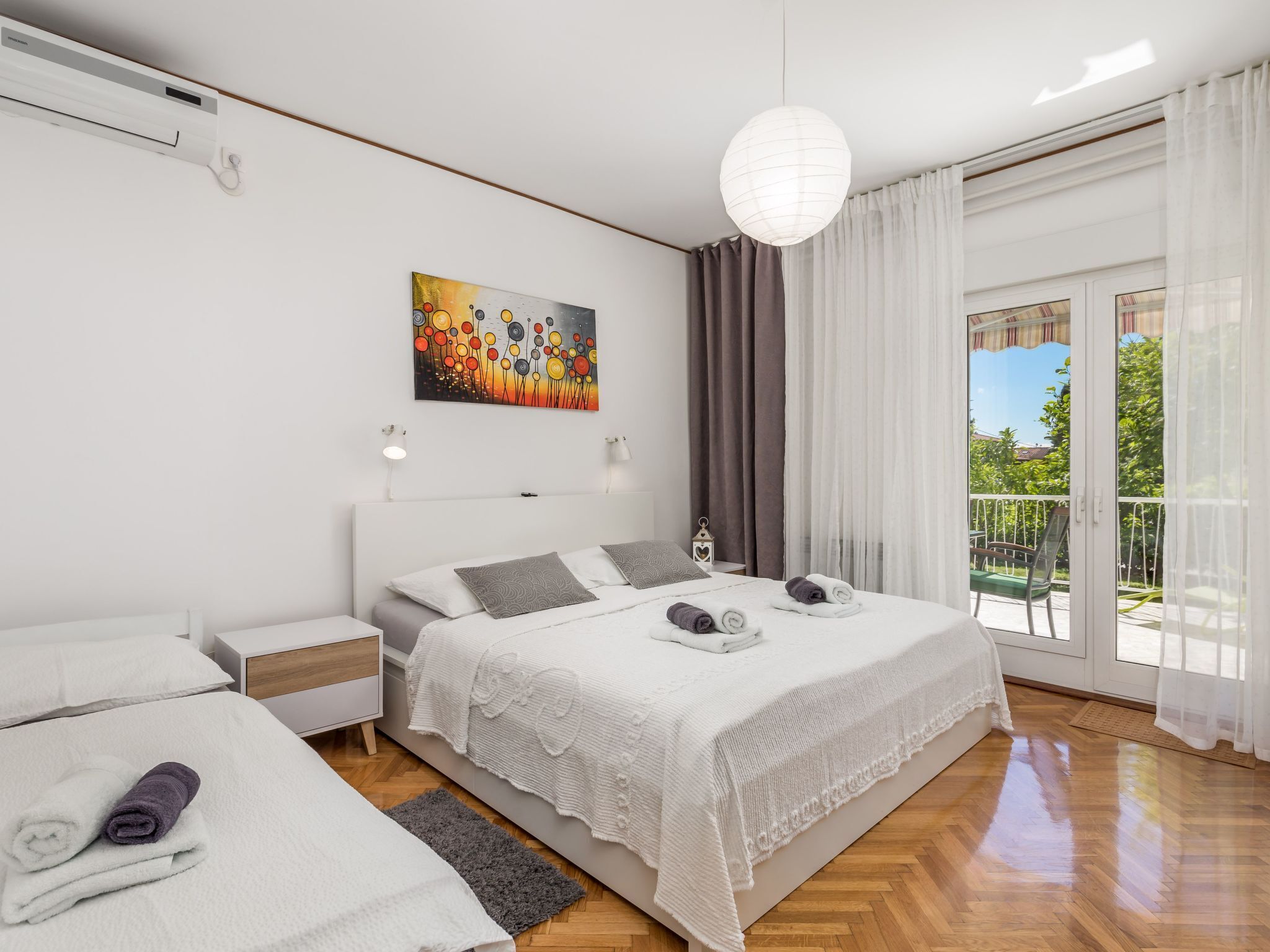 Ein modernes Schlafzimmer mit einem großen Bett, einem kleineren Bett, einem Gemälde und einem Balkon mit Vorhängen.