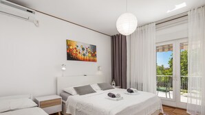 Un dormitorio moderno con una cama grande, una cama más pequeña, un cuadro y un balcón con cortinas.