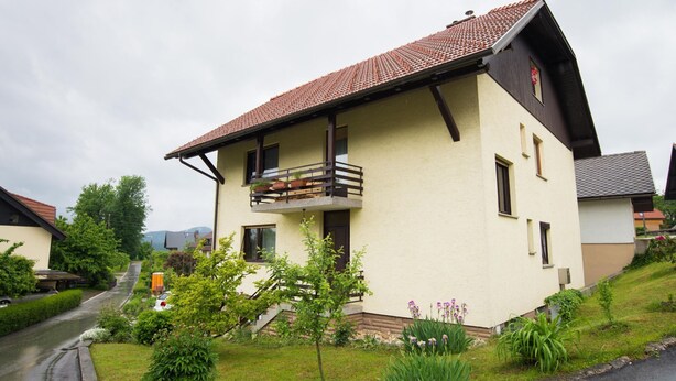 Ein zweistöckiges Haus mit Balkon, umgeben von Grünflächen und einem gepflasterten Auffahrt.