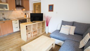 Ein modernes Wohnzimmer mit einem grauen Sofa, einem Holztisch und einem Fernseher auf einem Holzgestell.