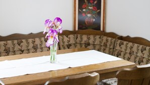 Ein Esstisch mit einer Vase voller lila Blumen, einem gerahmten Gemälde an der Wand und einem gepolsterten Sofa mit Blumenmuster.