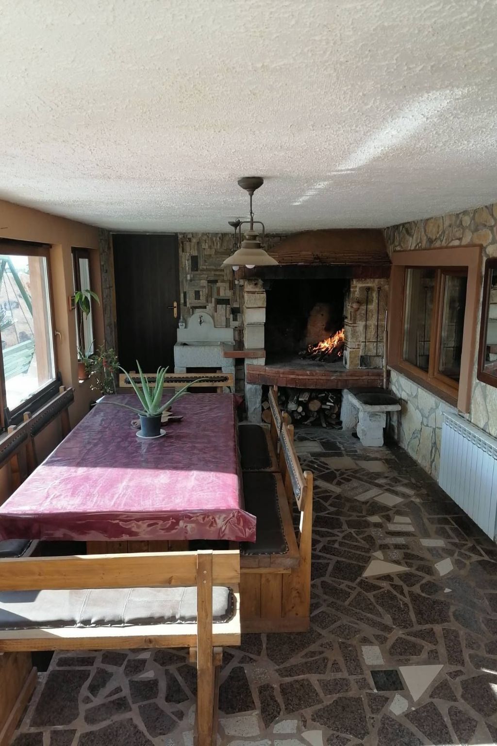 Una habitación acogedora con chimenea de piedra, un banco de madera y una mesa con mantel rosa.