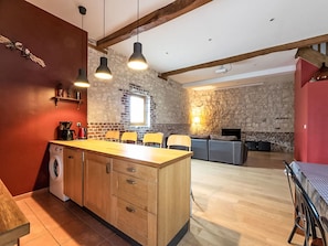 Une cuisine avec un îlot central en bois, un lave-linge et un coin repas avec des chaises.
