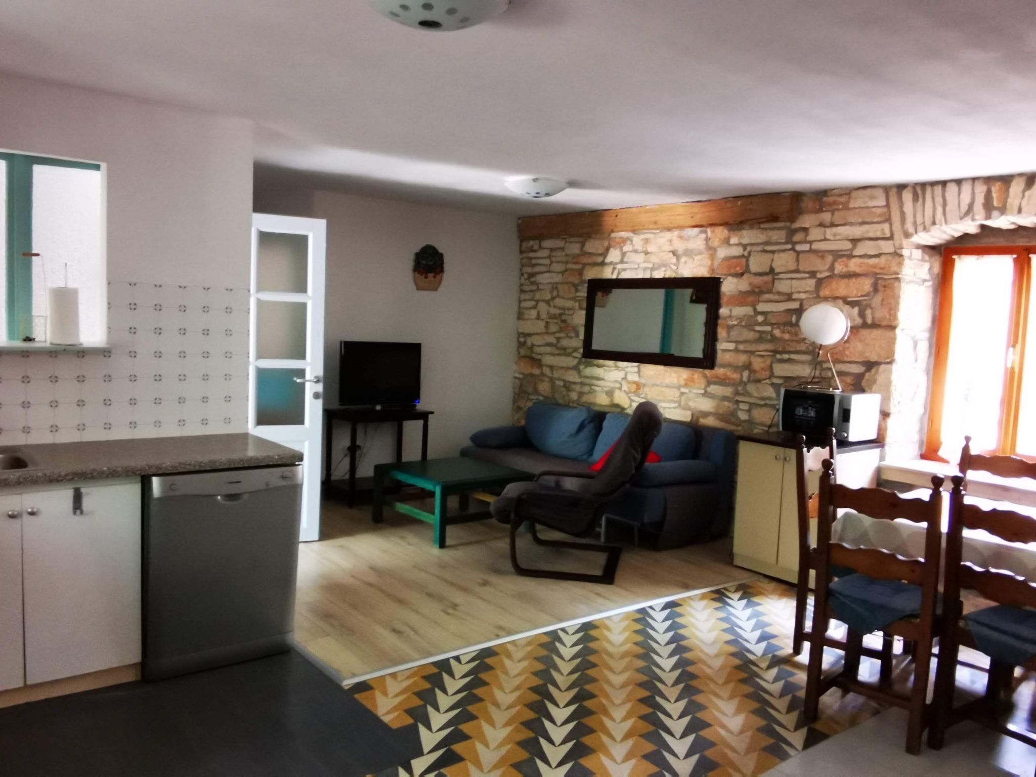 A compact living space with a kitchenette, a sofa, a dining table, and a stone accent wall.