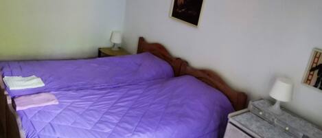A bedroom with a purple bedspread, a wooden headboard, two bedside tables with lamps, and a framed picture on the wall.