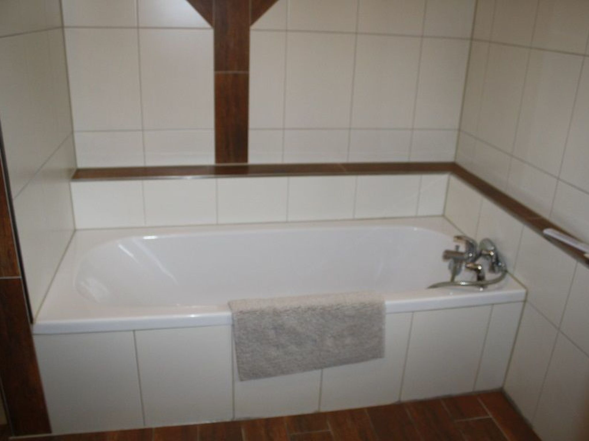 A bathroom with a white bathtub, a towel hanging on the side, and brown-tiled flooring.