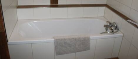 A bathroom with a white bathtub, a towel hanging on the side, and brown-tiled flooring.