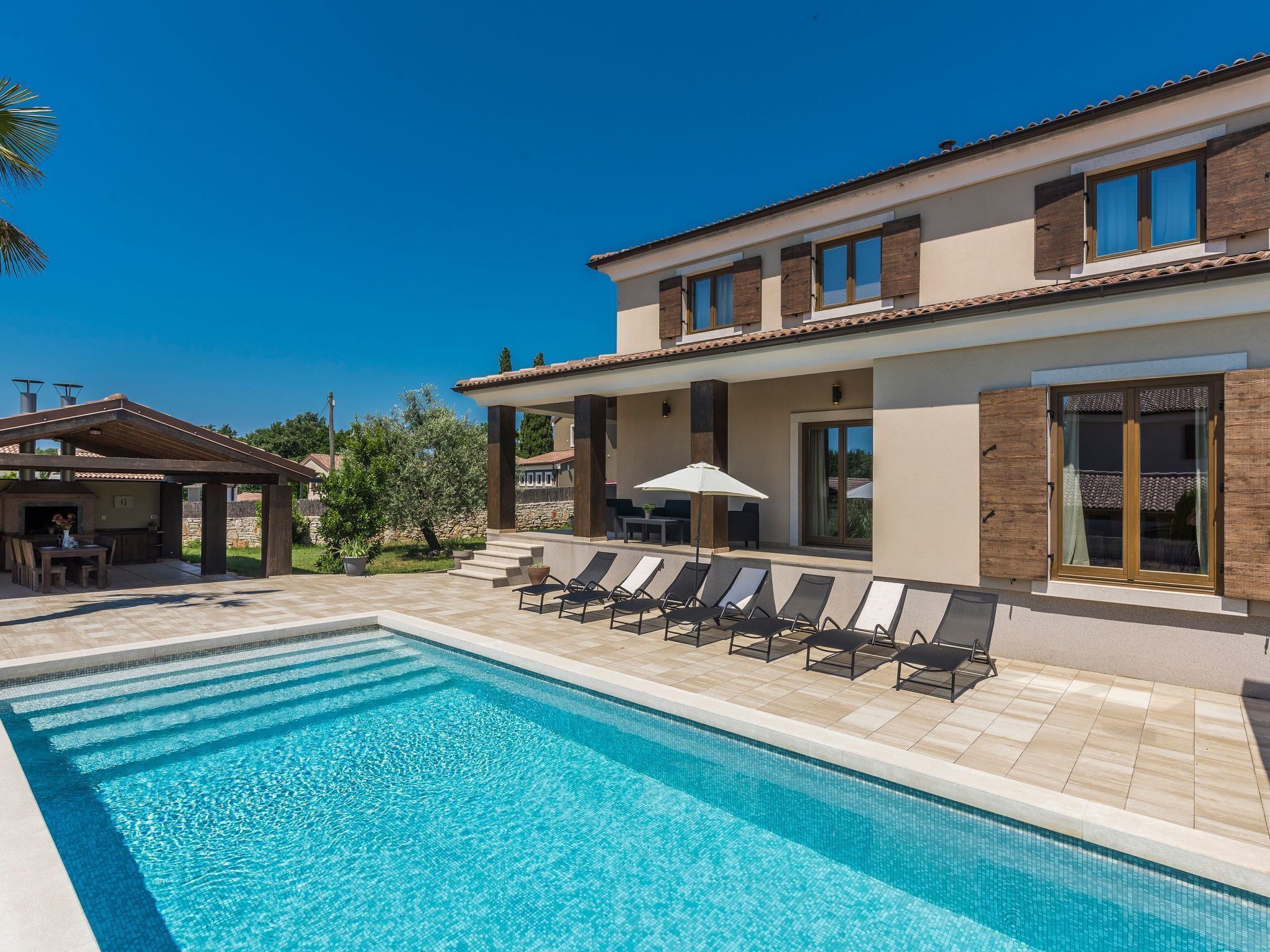 Uma casa moderna de dois andares com piscina, área de estar ao ar livre e um terraço coberto.