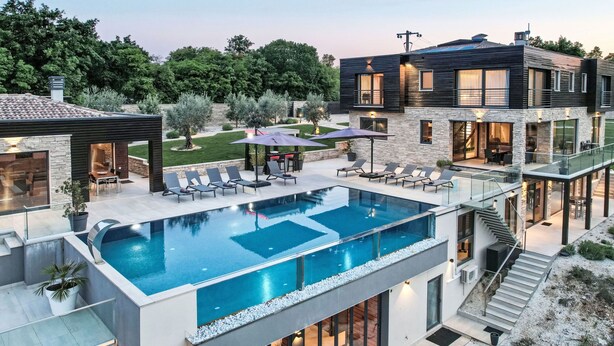 Una casa moderna amb piscina, mobiliari d'exterior i una escala cap a un balcó.