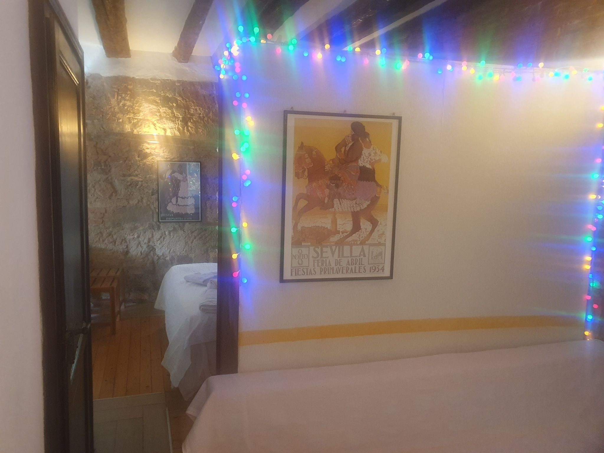 Une chambre avec un lit, une affiche encadrée au mur et des guirlandes lumineuses colorées.