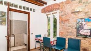Une pièce avec un plancher en bois, une table entourée de chaises, une fenêtre donnant sur un paysage verdoyant et une affiche accrochée au mur.