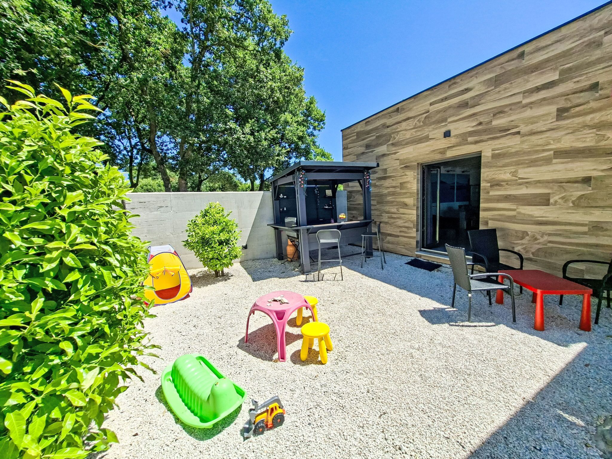 Un espace patio aménagé avec un barbecue, des sièges d’extérieur et un petit coin de jeux pour les enfants.