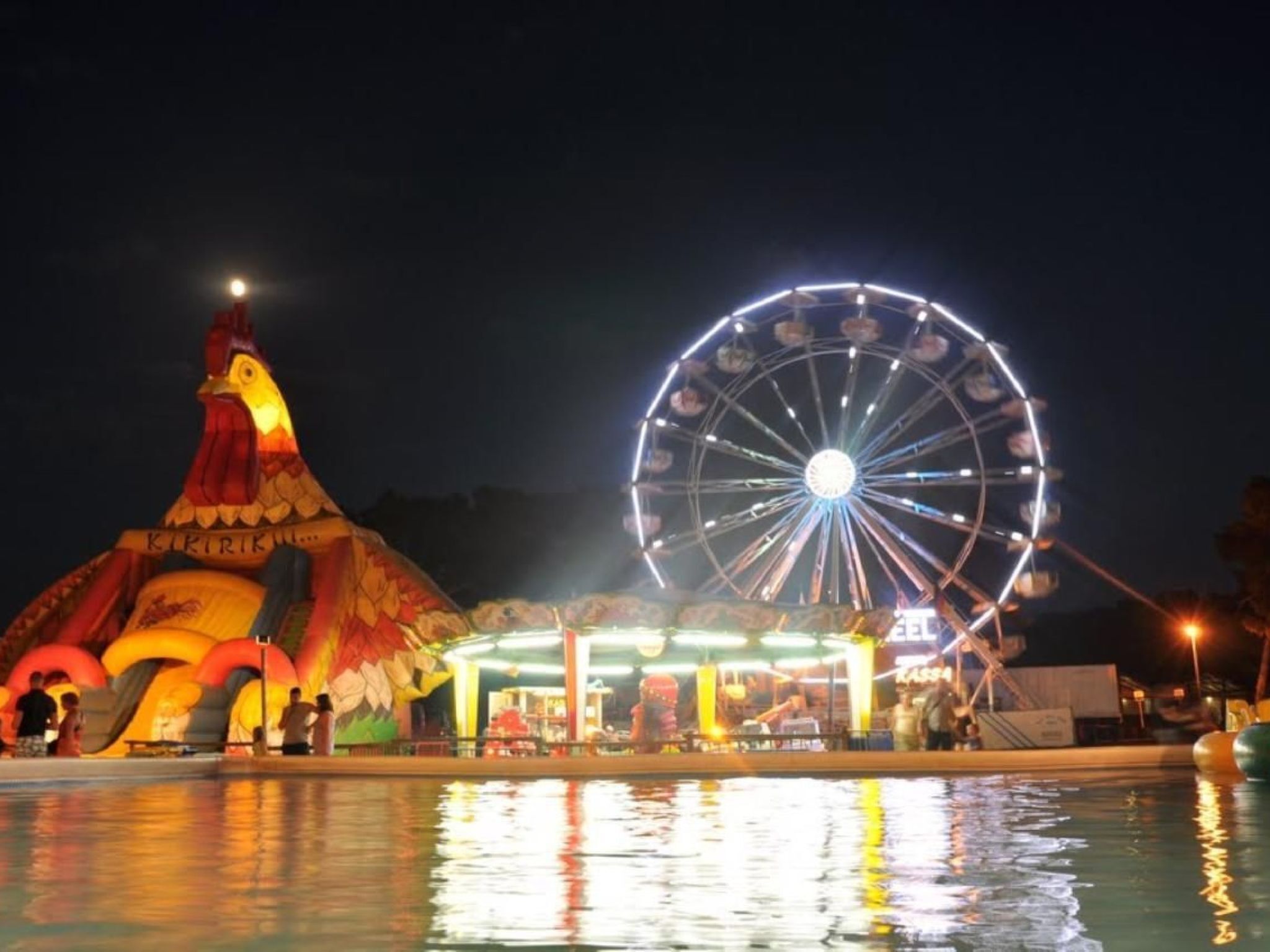 A Ferris wheel and a colorful inflatable structure at a nighttime amusement park.