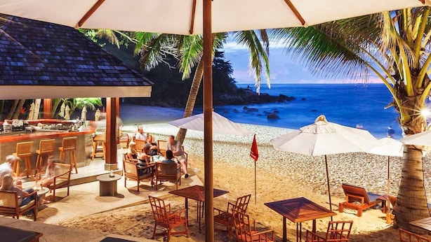 A beachside bar with outdoor seating and umbrellas, overlooking a sandy beach with palm trees and the ocean. - Wellness und Spa Villa Stella, in der Nähe von Stränden - Meer by Interhome (Bokordici)