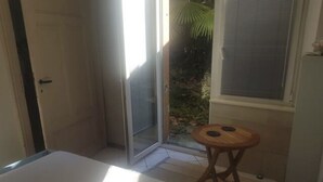 Una camera da letto con un letto, una porta scorrevole in vetro che dà su un balcone e uno sgabello di legno.
