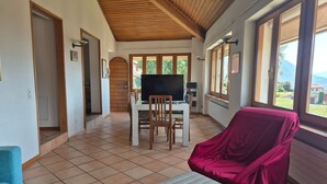 A spacious room with a tiled floor, a wooden ceiling, a dining table with chairs, a television, and a covered chair. - Executive mit 6 Schlafzimmern und 2 Bädern by Interhome (Lugano)