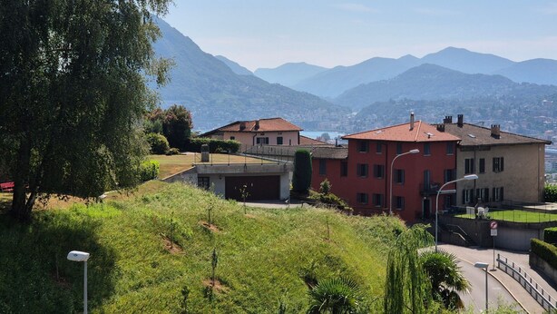 A hillside residential area with houses, a street, and mountains in the background. - Executive mit 6 Schlafzimmern und 2 Bädern by Interhome (Lugano)